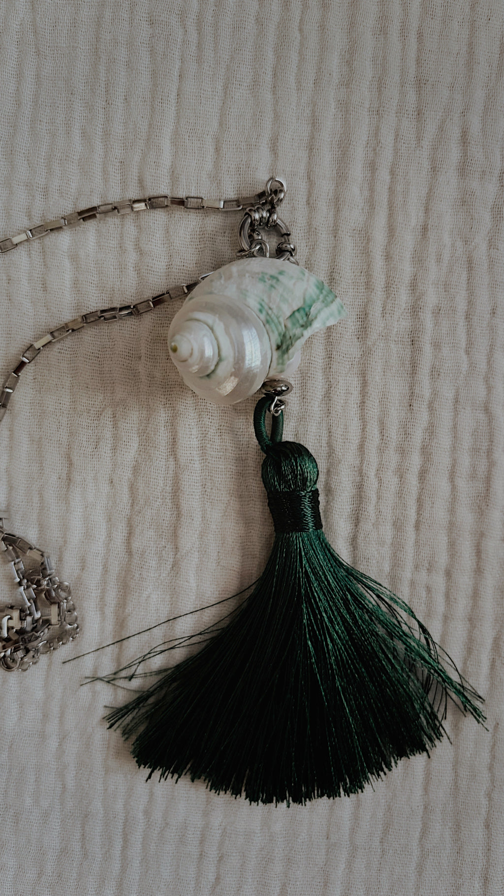 Teal mottled spiral shell with forest green silk tassel flat lay on fabric
