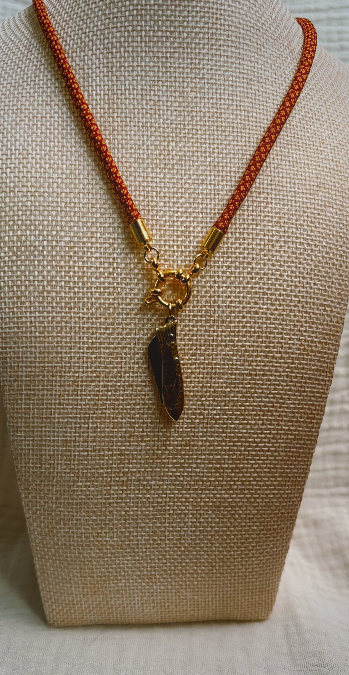 Dark shell fragment pendant on orange patterned paracord