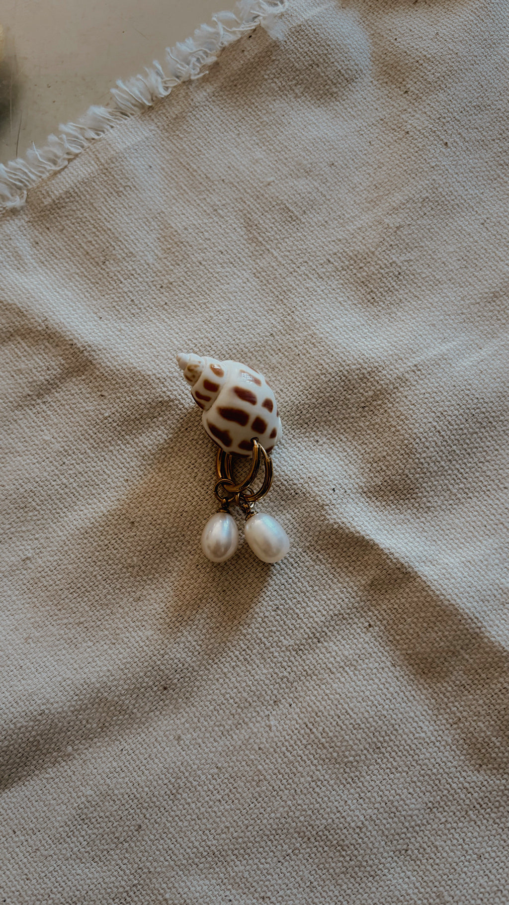 Gold hoop earrings with teardrop pearl drops on spotted spiral shell