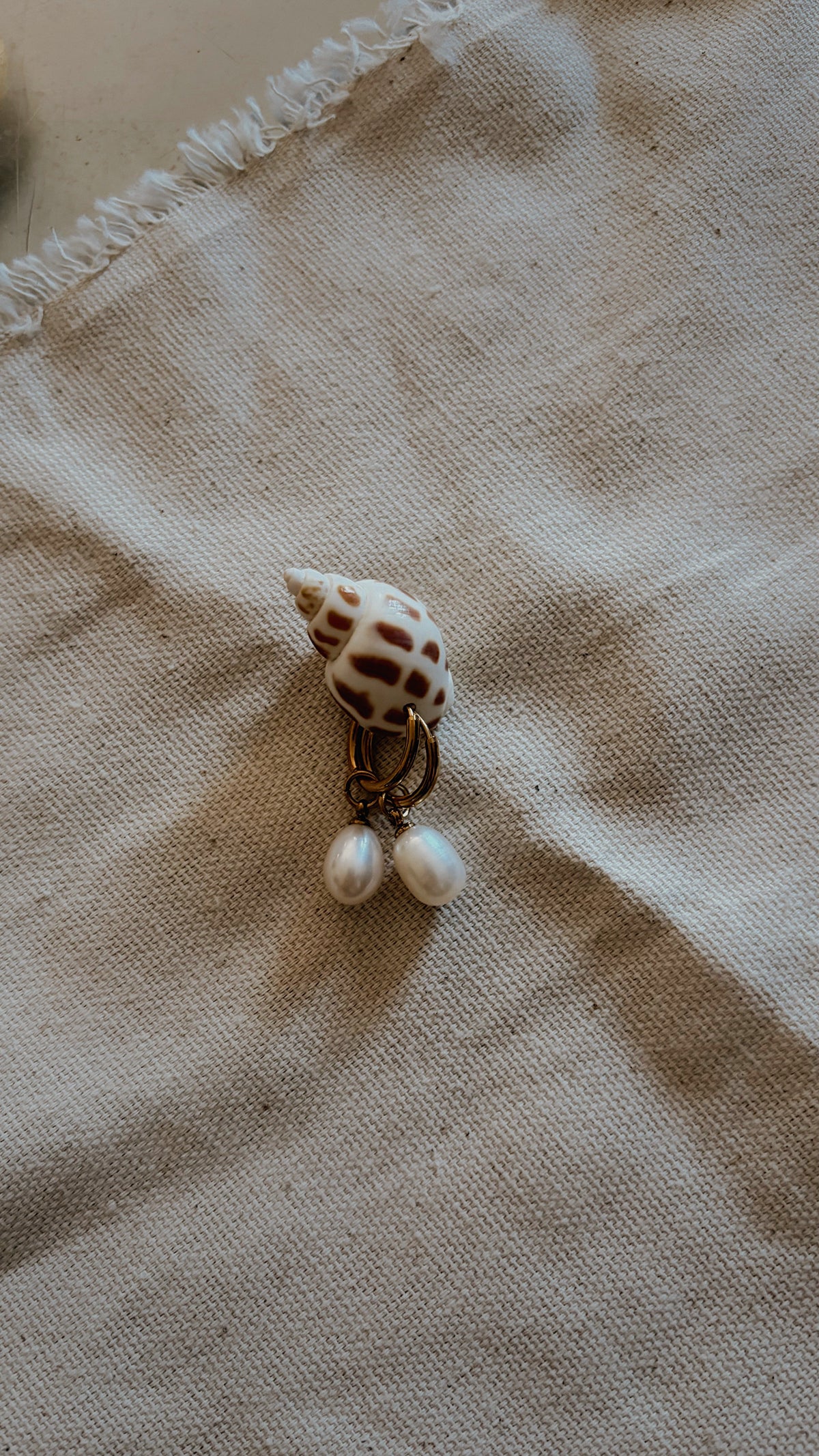 Gold hoop earrings with teardrop pearl drops on spotted spiral shell
